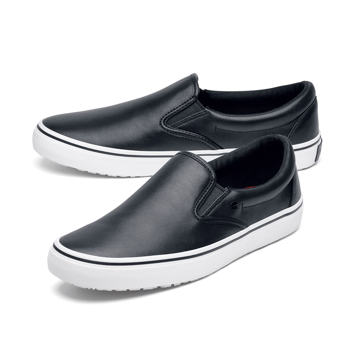 The Merlin Slip On Black and White from Shoes For Crews are slip-on trainers that are slip-resistant, lightweight, easy to clean and water-resistant, pair seen from the left side, emphasised on the tip of the left shoe.