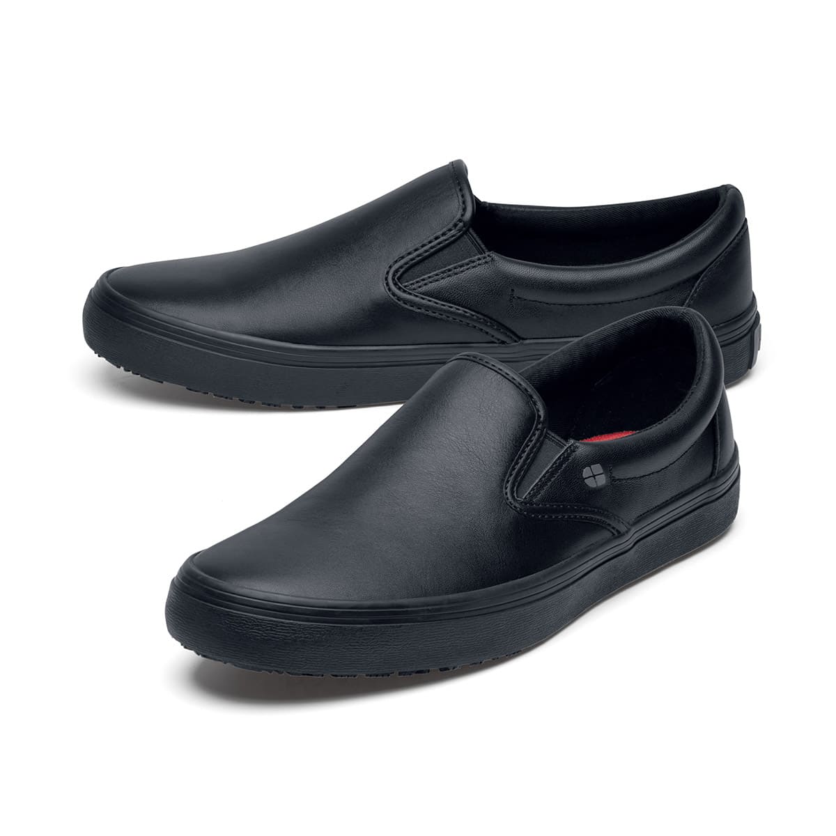 The Merlin Black from Shoes For Crews are slip-on slip resistant shoes with a lightweight design and constructed from genuine leather that has been specially treated to repel liquids from the surface, pair seen from the left side, emphasised on the tip of the left shoe.